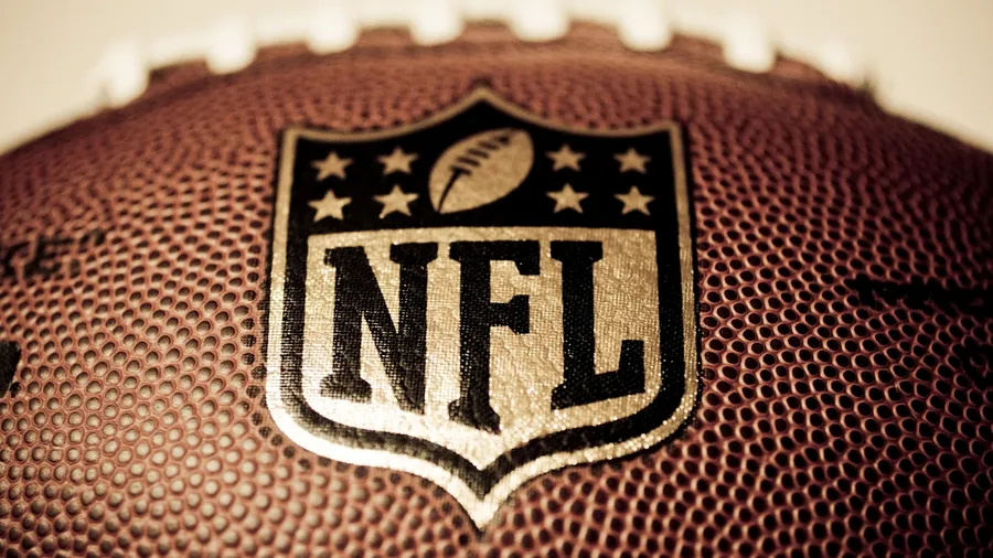 A cool close-up shot of a printed NFL logo on a brown football with a blurry background. A cool close-up shot of a printed NFL logo on a brown football with a blurry background.